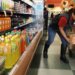 Grocery store employee placing containers of fruit on a cart in the beverage aisle.