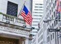 Exterior view of the New York Stock Exchange building featuring an American flag and street signs.