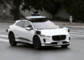 White Waymo autonomous vehicle with sensors and cameras parked on a city street.