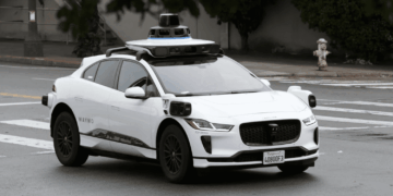 White Waymo autonomous vehicle with sensors and cameras parked on a city street.