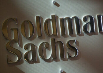 Metallic sign displaying the name 'Goldman Sachs' in a corporate setting.