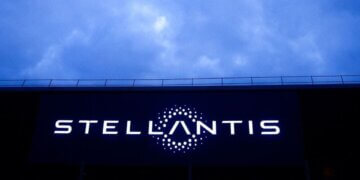 Stellantis logo illuminated on a large screen against a cloudy sky.