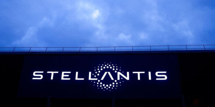 Stellantis logo illuminated on a large screen against a cloudy sky.