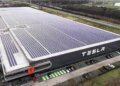 Aerial view of the Tesla factory in Tilburg featuring solar panels on the roof and the Tesla logo on the side.