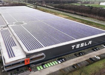 Aerial view of the Tesla factory in Tilburg featuring solar panels on the roof and the Tesla logo on the side.