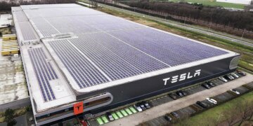 Aerial view of the Tesla factory in Tilburg featuring solar panels on the roof and the Tesla logo on the side.