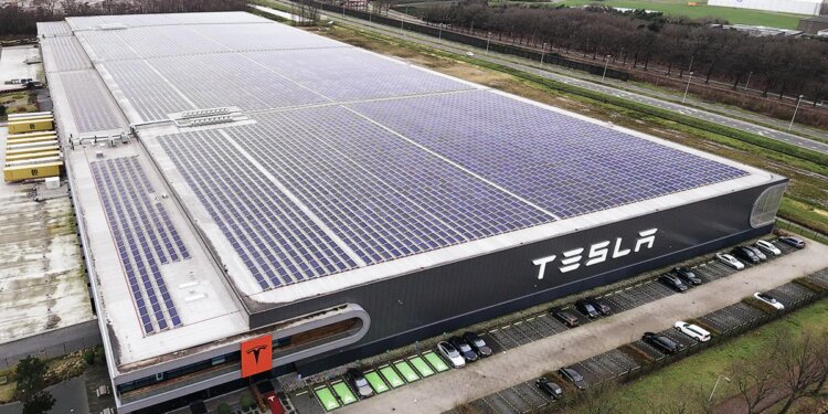 Aerial view of the Tesla factory in Tilburg featuring solar panels on the roof and the Tesla logo on the side.