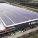 Aerial view of the Tesla factory in Tilburg featuring solar panels on the roof and the Tesla logo on the side.