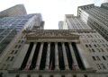 Facade of the New York Stock Exchange with columns and flags, viewed from below.