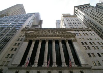 Facade of the New York Stock Exchange with columns and flags, viewed from below.