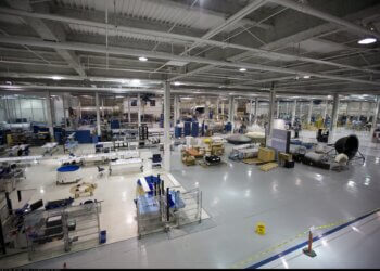 Interior view of a large manufacturing facility with various equipment and workstations.
