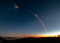 A rocket launch trail creating a bright arc in the evening sky against a gradient backdrop.