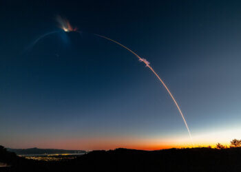A rocket launch trail creating a bright arc in the evening sky against a gradient backdrop.