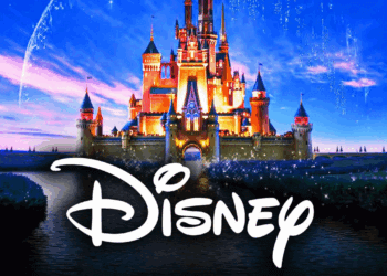 Illuminated Disney castle with the Disney logo in front of a blue sky background.