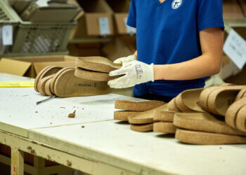 Person assembling cork footwear on a work table with several pairs visible.