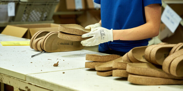 Person assembling cork footwear on a work table with several pairs visible.