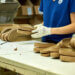 Person assembling cork footwear on a work table with several pairs visible.
