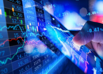 A hand pointing at a digital display of stock market data with graphs and numbers.