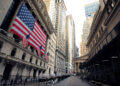 Facade of the New York Stock Exchange featuring large American flags and surrounding skyscrapers.