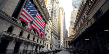 Facade of the New York Stock Exchange featuring large American flags and surrounding skyscrapers.