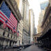 Facade of the New York Stock Exchange featuring large American flags and surrounding skyscrapers.